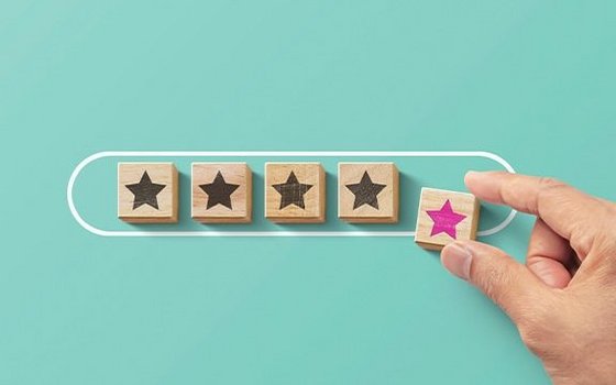 4 Holzplättchen mit einem schwarzen Stern, eine Hand legt ein weiteres mit einem pinken Stern dazu.