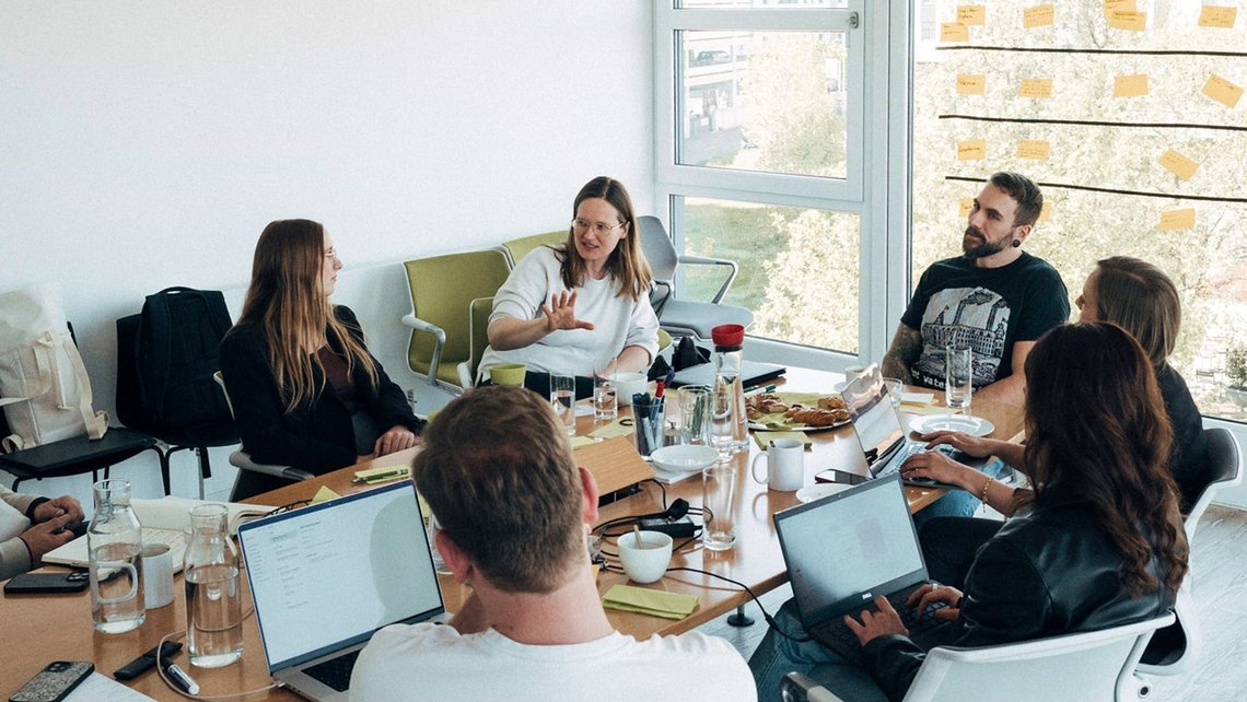 Mehrere Personen sitzen mit Laptops in einem Meeting